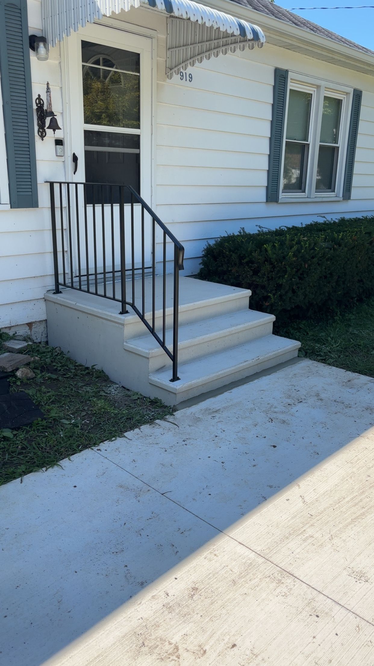 Concrete steps leading to a white house with black railing, light blue shutters, and a front door.
