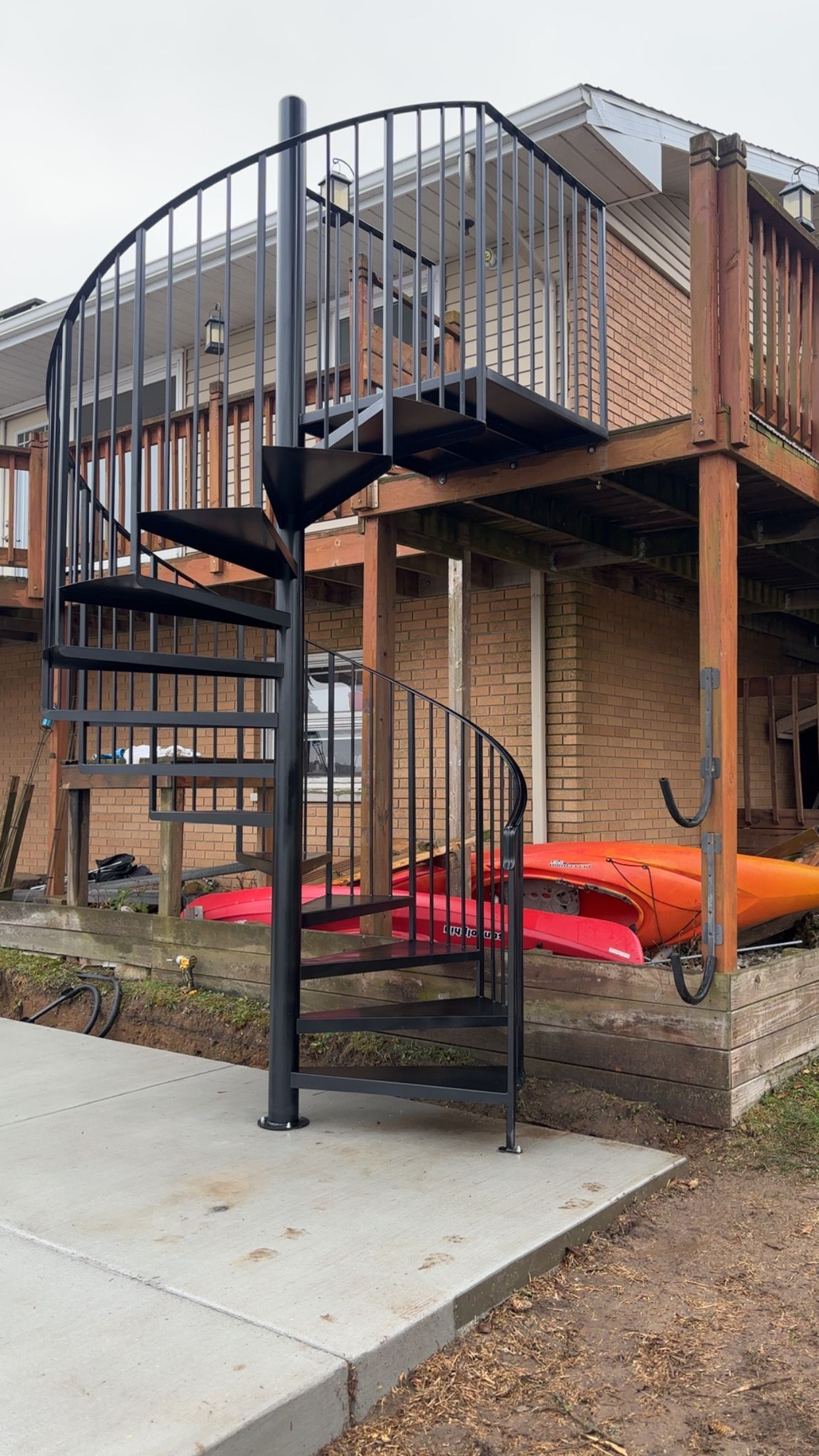Black spiral staircase leading up to a wooden deck on a brick building exterior.