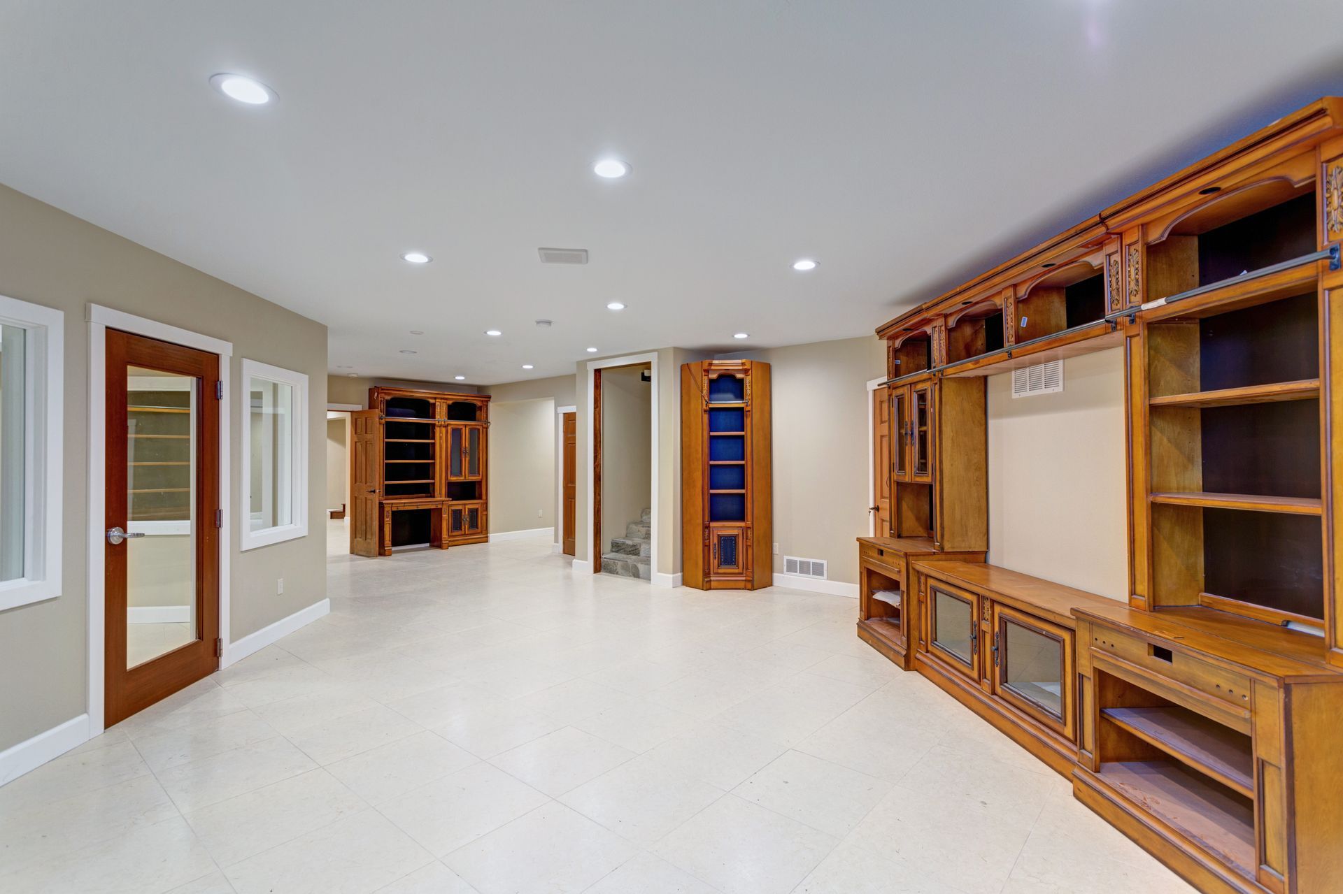 Empty, light-colored basement with built-in wooden cabinetry on the right and a door on the left.
