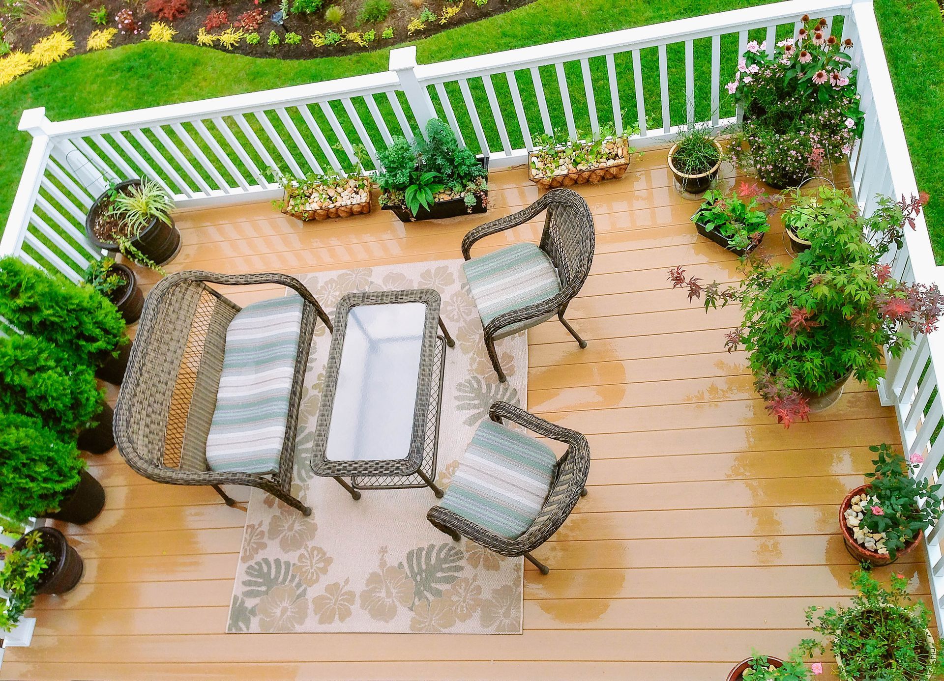 Wooden deck with wicker furniture and potted plants, overlooking a green lawn.