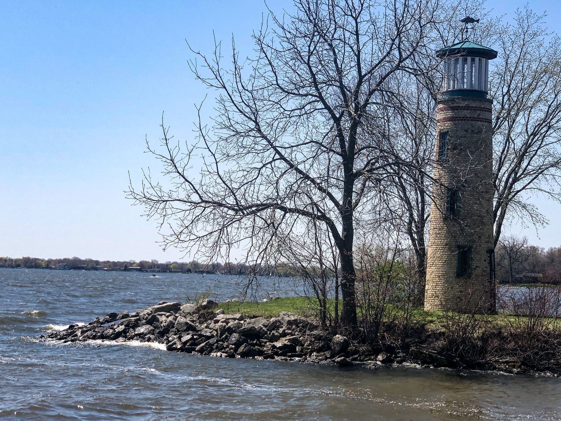 Brick lighthouse on a small peninsula by a lake, with bare trees and a clear blue sky. Brick lighthouse on a small peninsula by a lake, with bare trees and a clear blue sky.