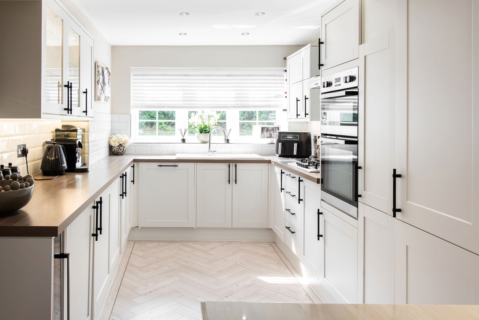 White kitchen with light wood countertops, black hardware, and a window above the sink.