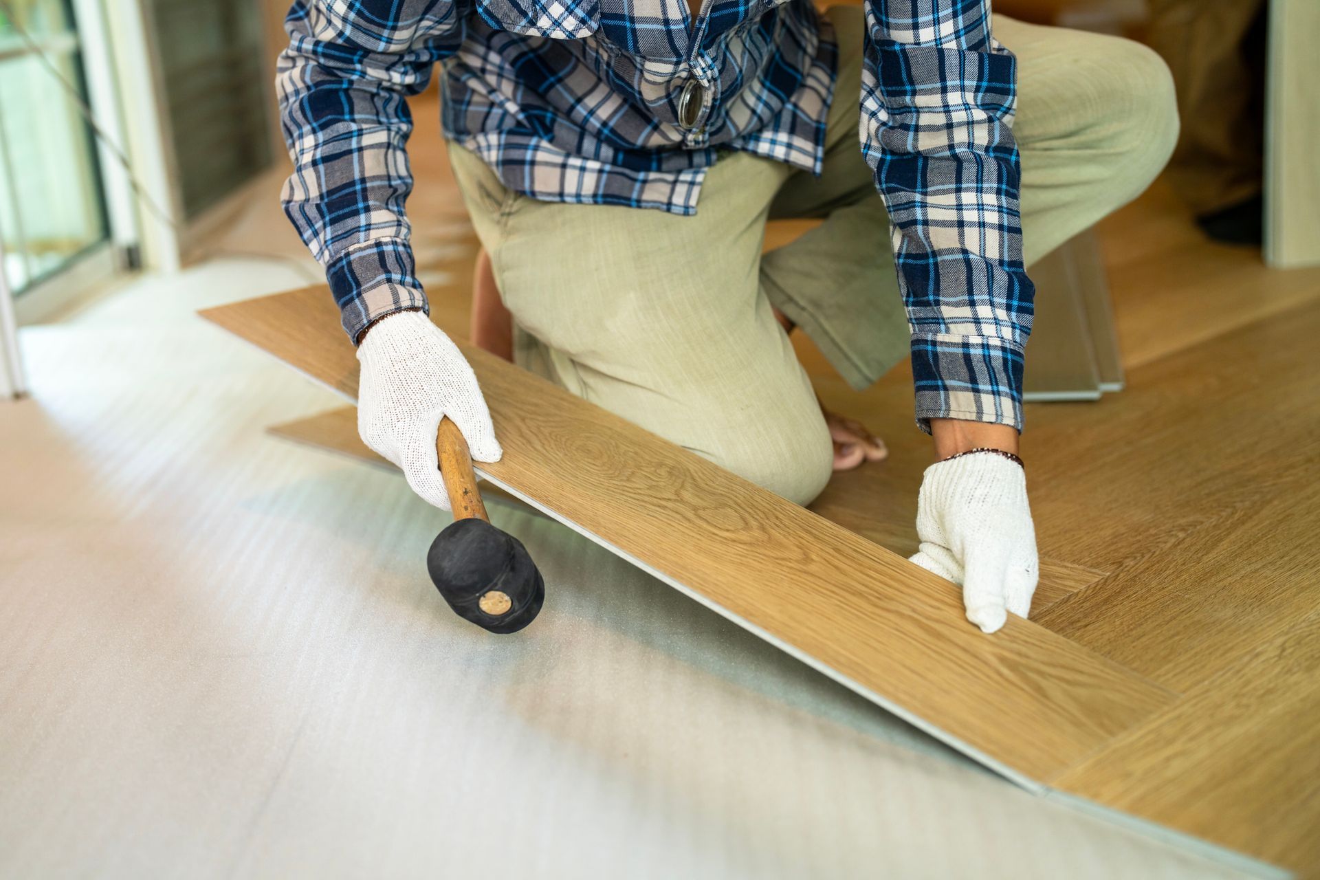 Person installing wood-look flooring, kneeling and using a rubber mallet to secure a plank. Person installing wood-look flooring, kneeling and using a rubber mallet to secure a plank.