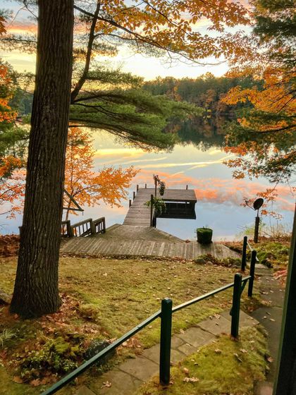 Wooden dock extending into calm lake, surrounded by autumn trees with orange and yellow leaves. Wooden dock extending into calm lake, surrounded by autumn trees with orange and yellow leaves.