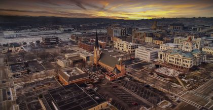 Aerial view of a city at sunset; buildings, church with spire, golden sky.