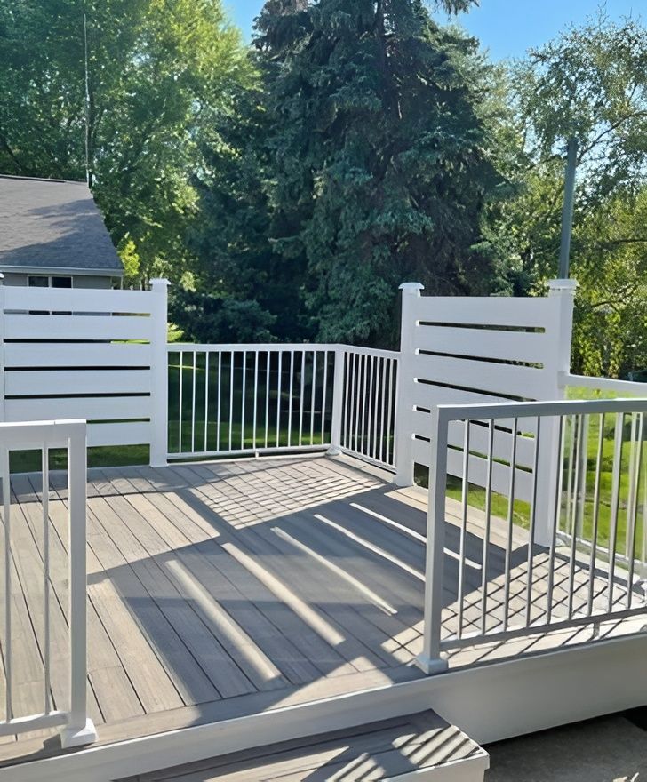 White deck with gray composite boards, white railing and horizontal fence panels, surrounded by trees.