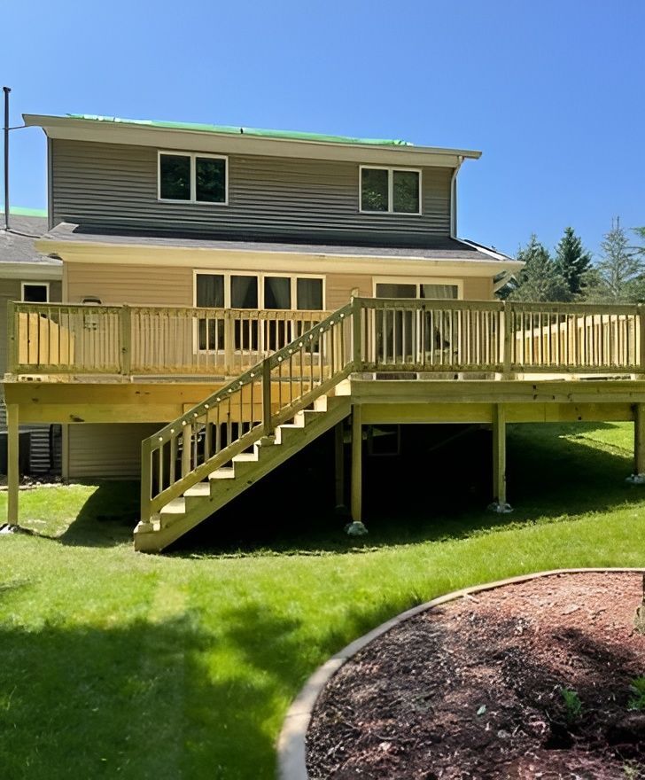 Newly built wooden deck with stairs attached to a two-story beige house with green lawn.