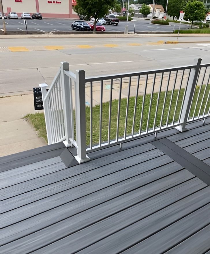 Gray composite deck with white railing, steps leading to street view with cars and stores.