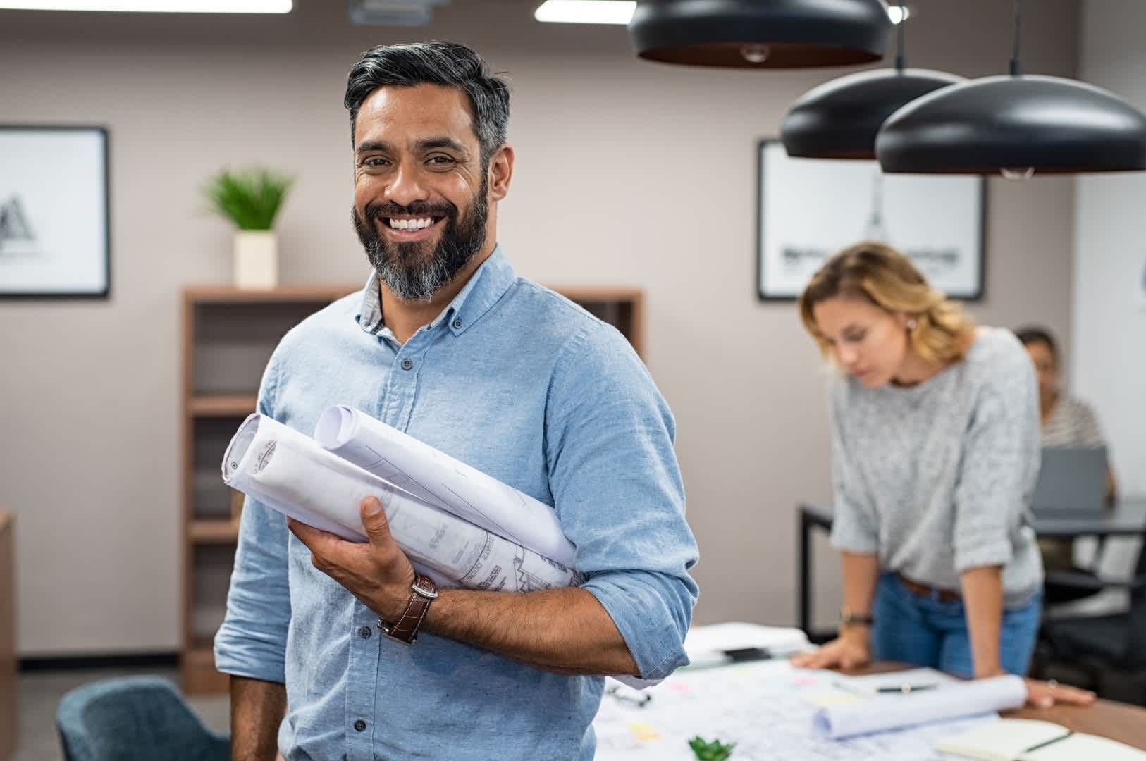 Man holding blueprints smiles in office setting.