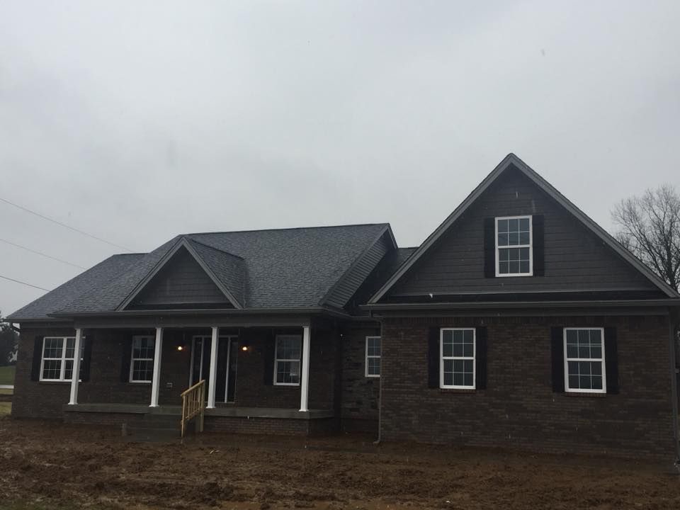 A newly built dark-brick house with a gray roof and a front porch under a cloudy sky.