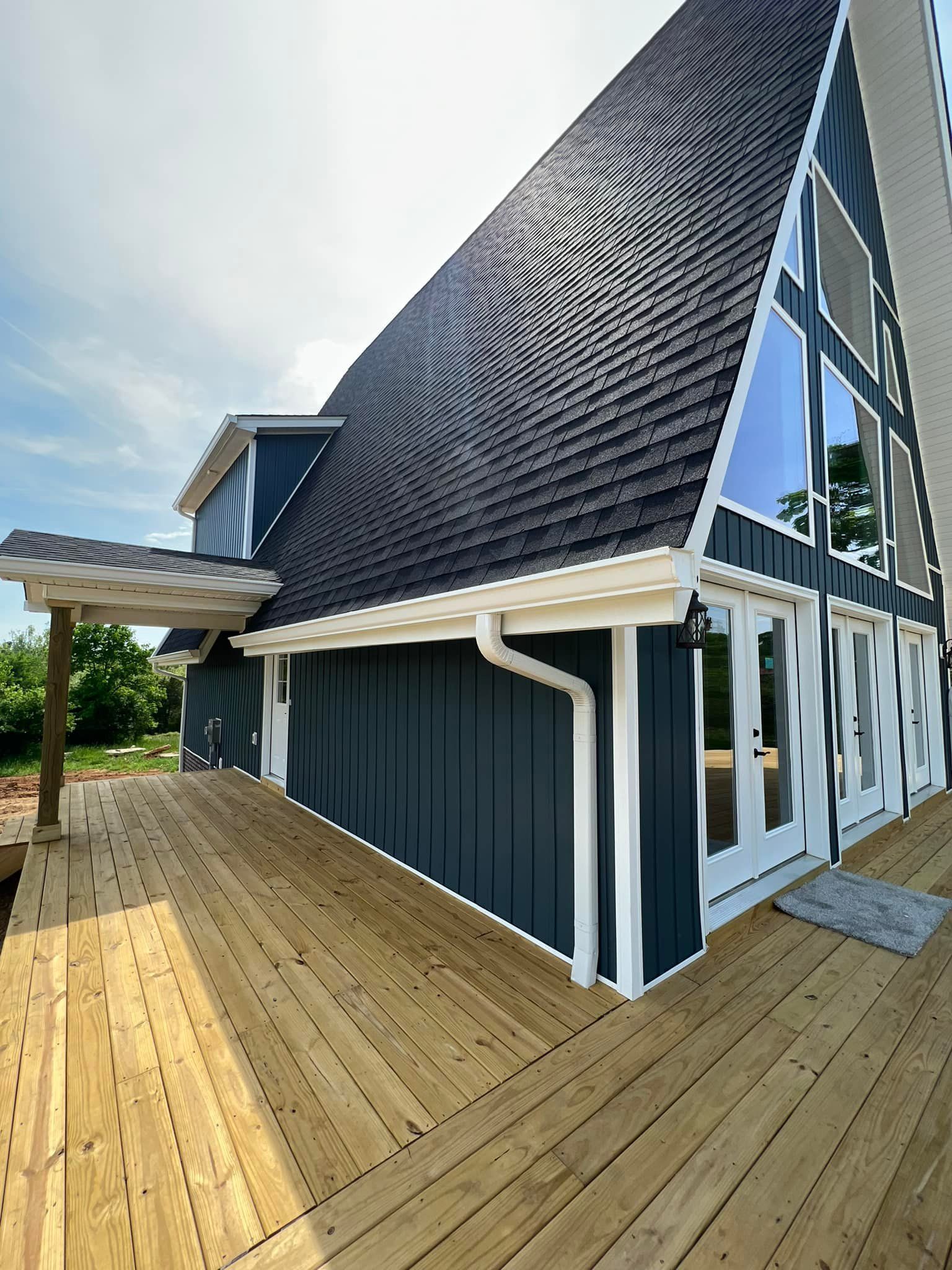 A dark blue A-frame house with a large wooden deck and white trim under a clear sky.