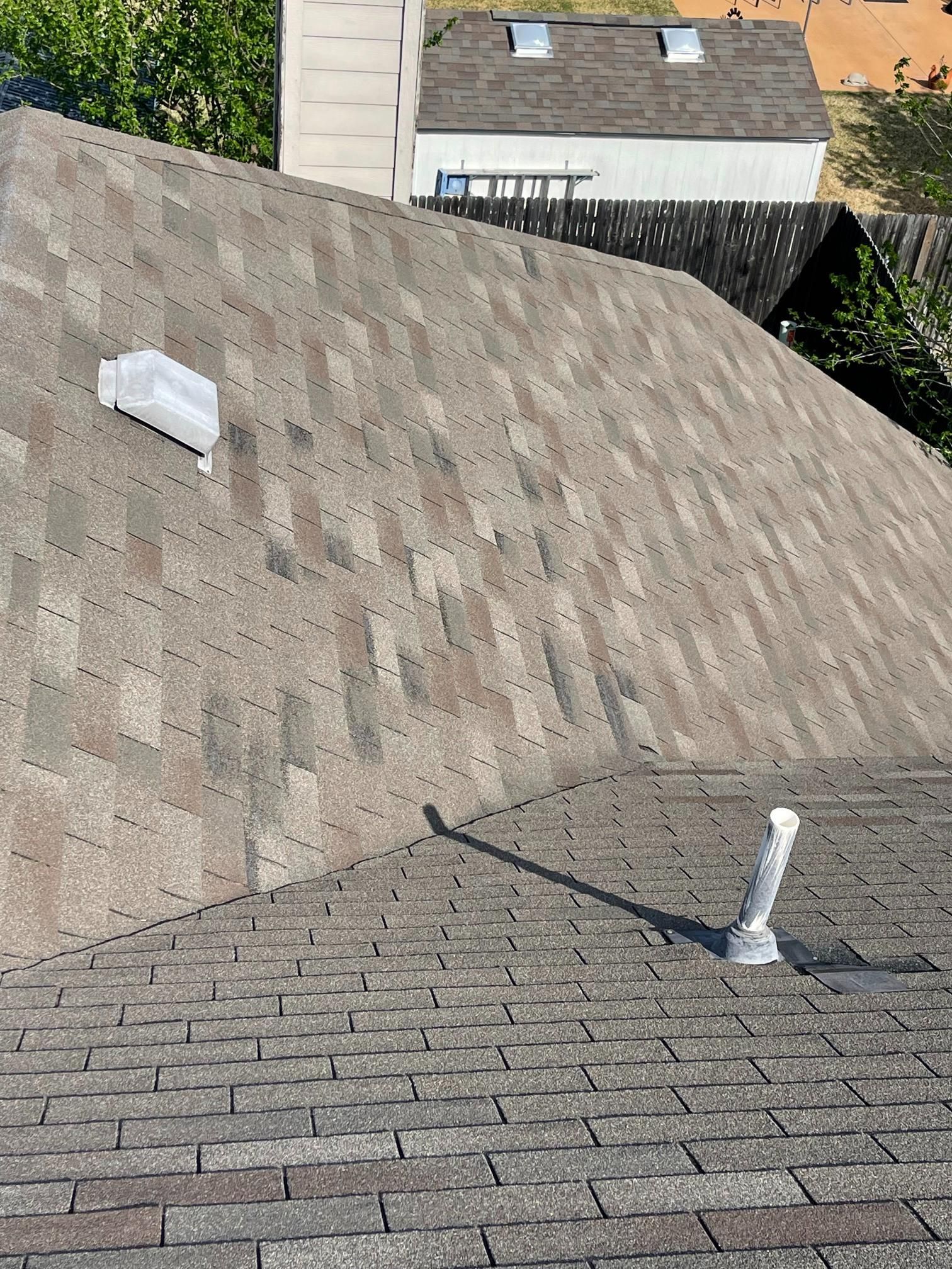 A close up of a roof with shingles and a pipe on it.