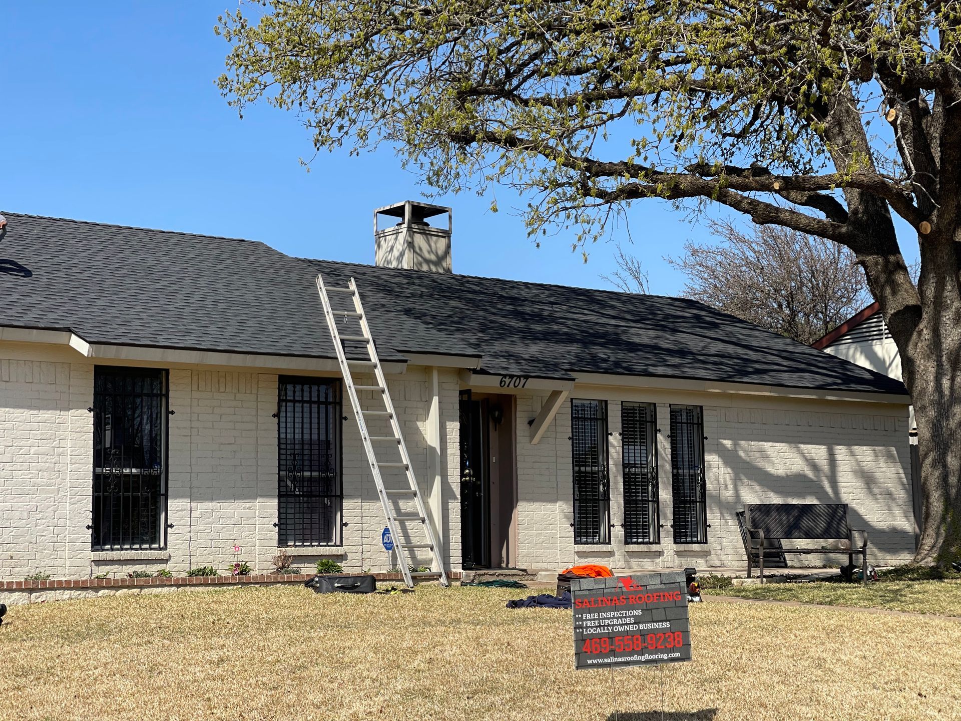 A house with a ladder on the roof and a sign in front of it.