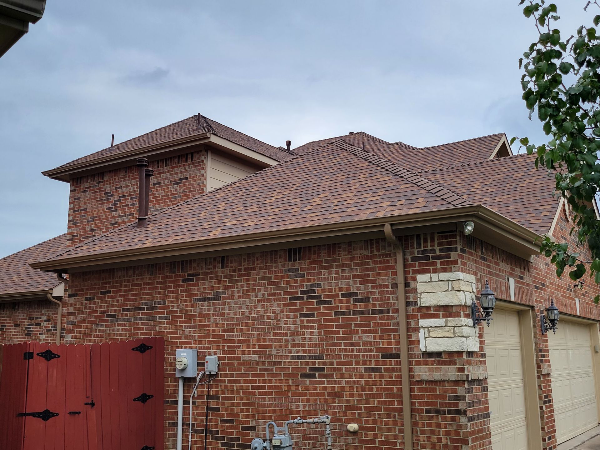 A brick house with a brown roof and a red garage door.