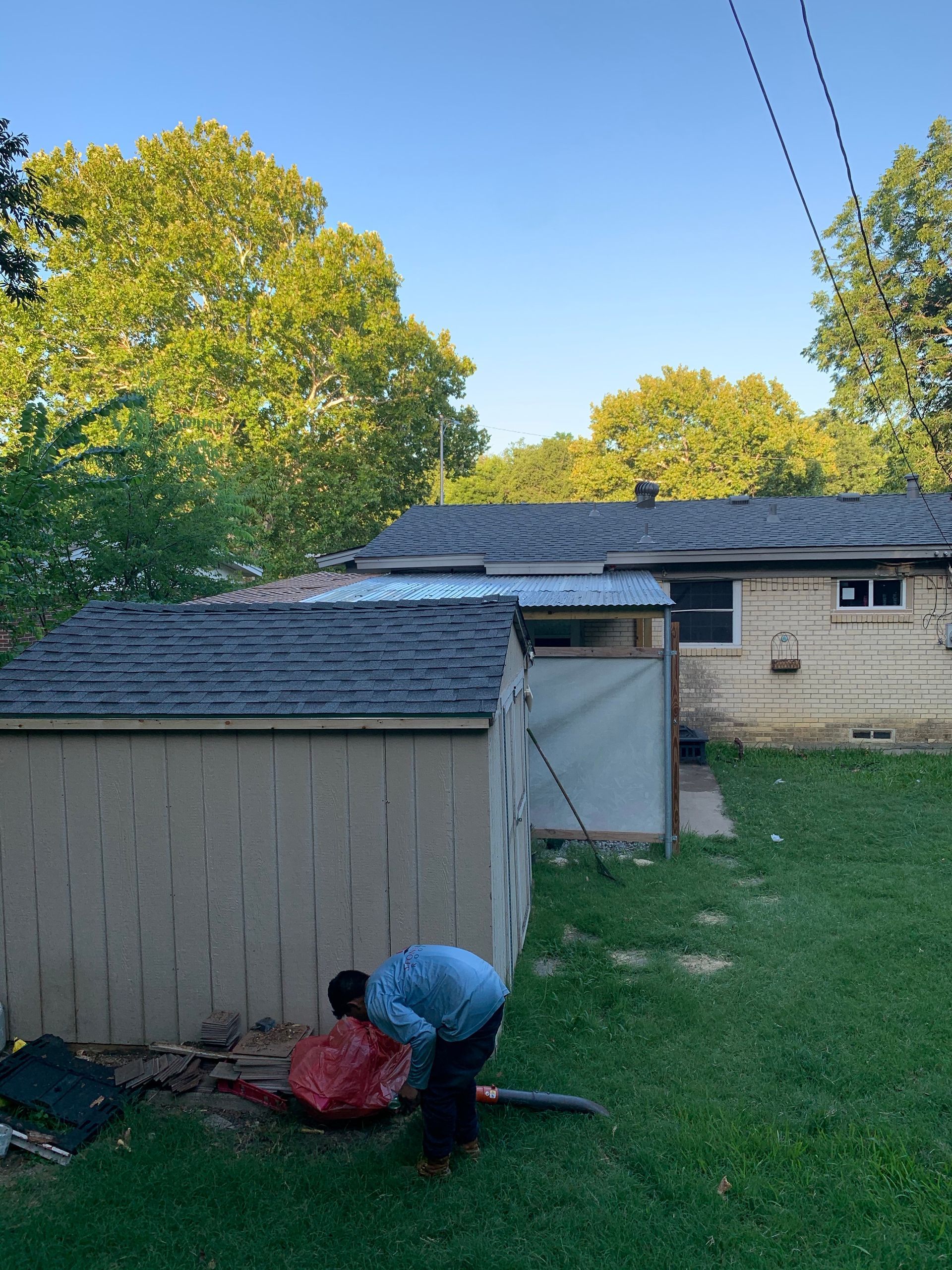A man is kneeling down in front of a shed in a backyard.