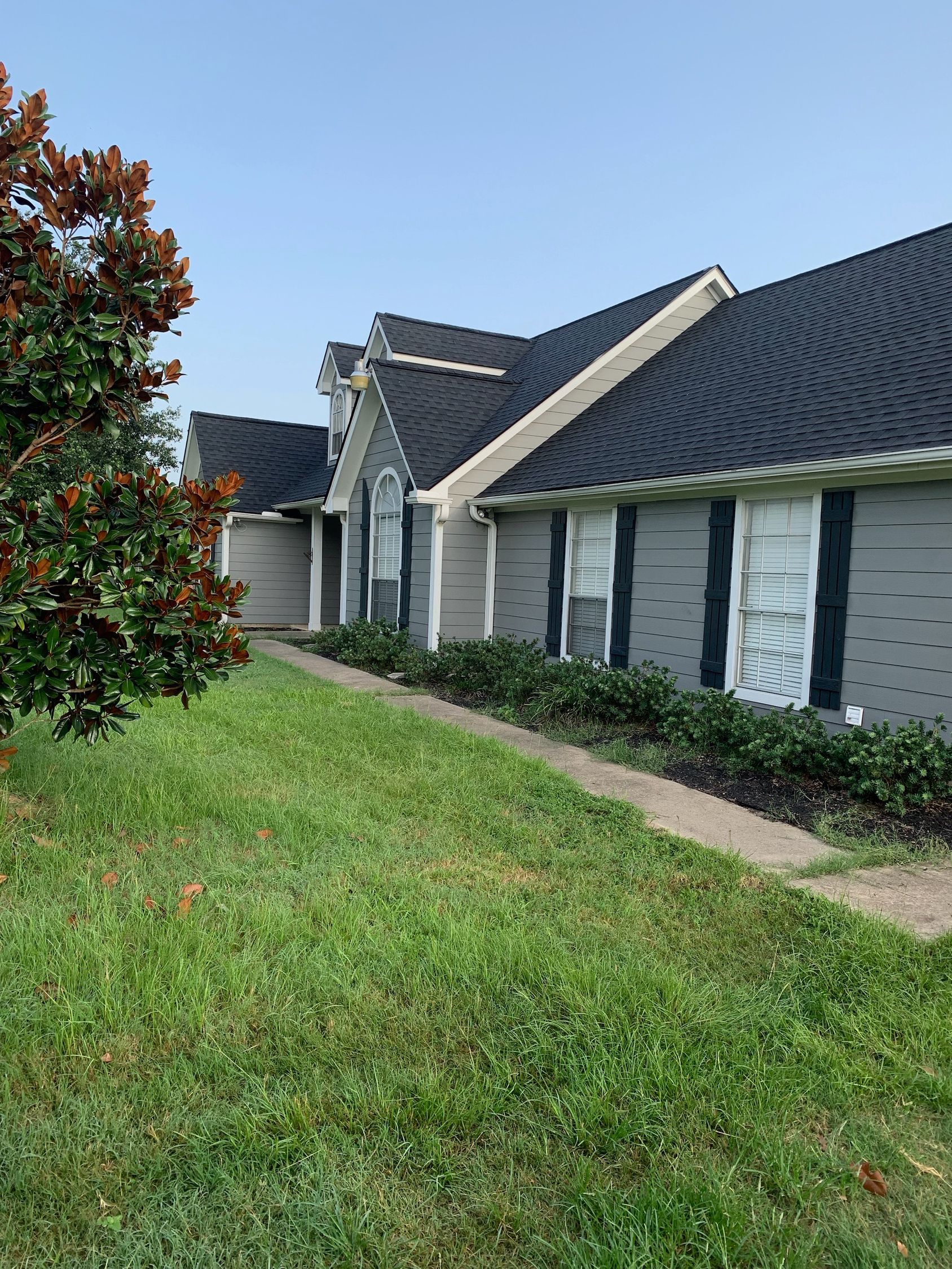 A house with a black roof is sitting on top of a lush green lawn.