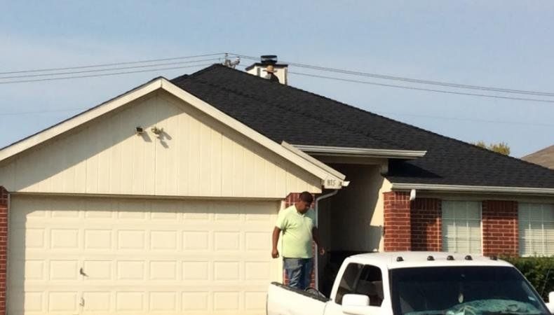 A man is standing on the back of a truck in front of a house.