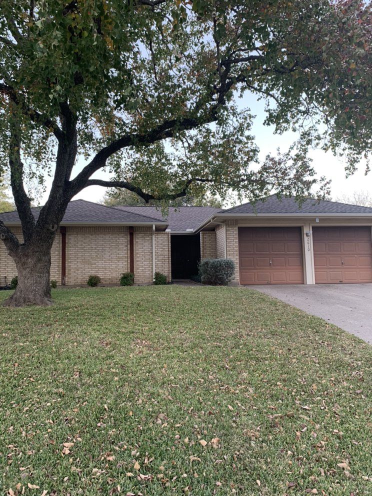 A house with three garage doors and a large tree in front of it.