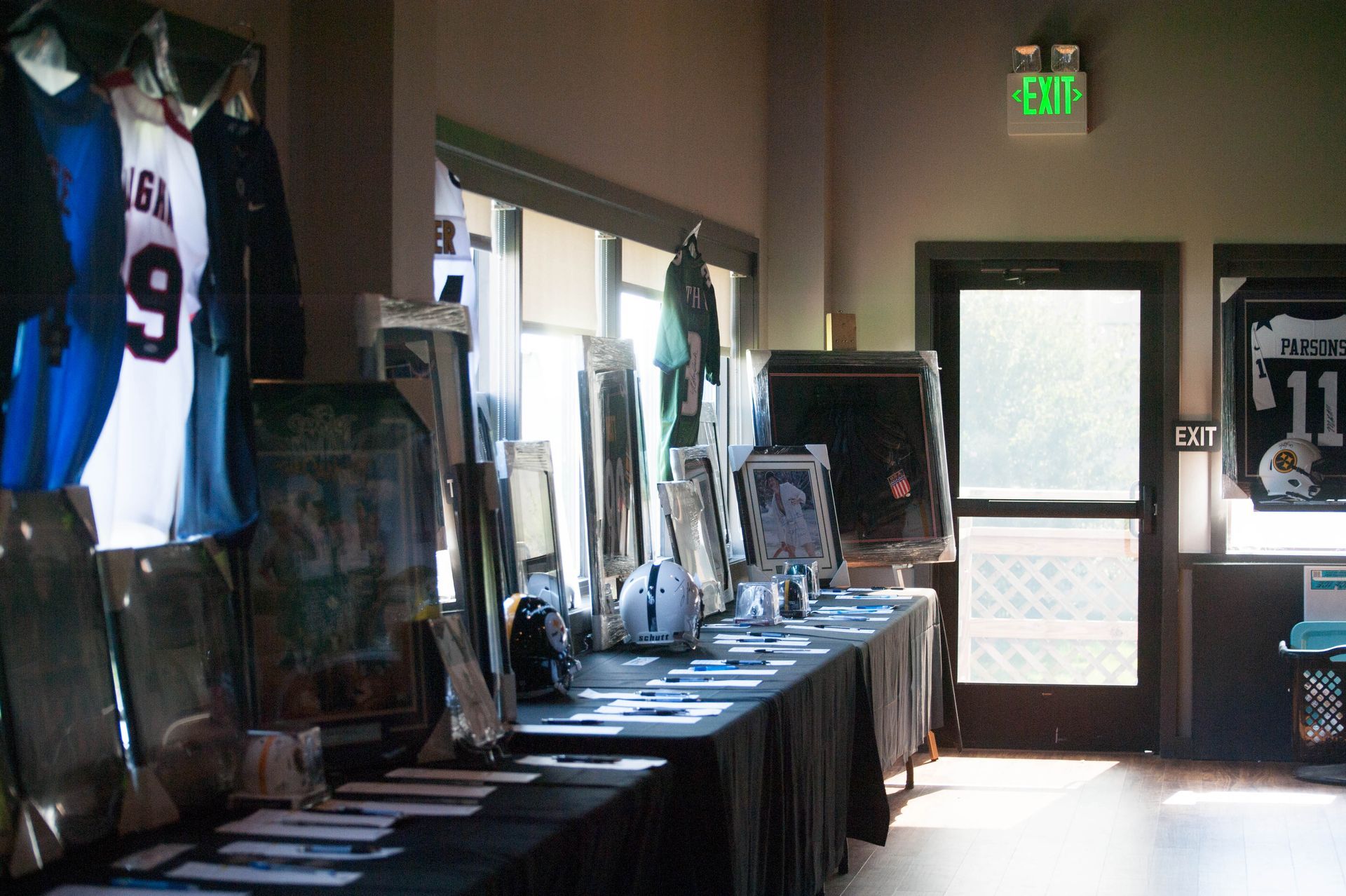 A room with a green exit sign and jerseys hanging on the wall