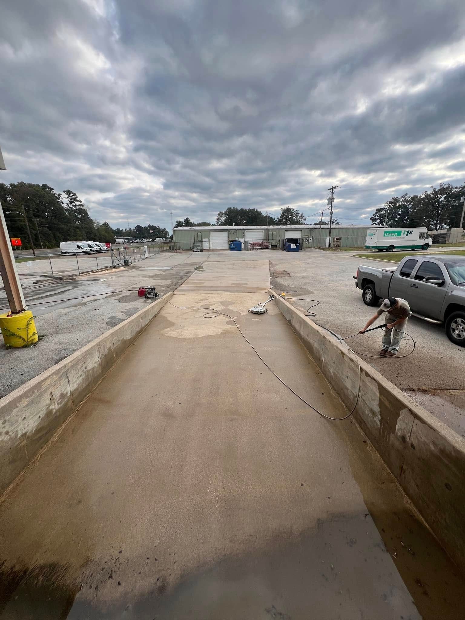 A concrete wash bay, with a person spraying down a truck in a parking lot under a cloudy sky.