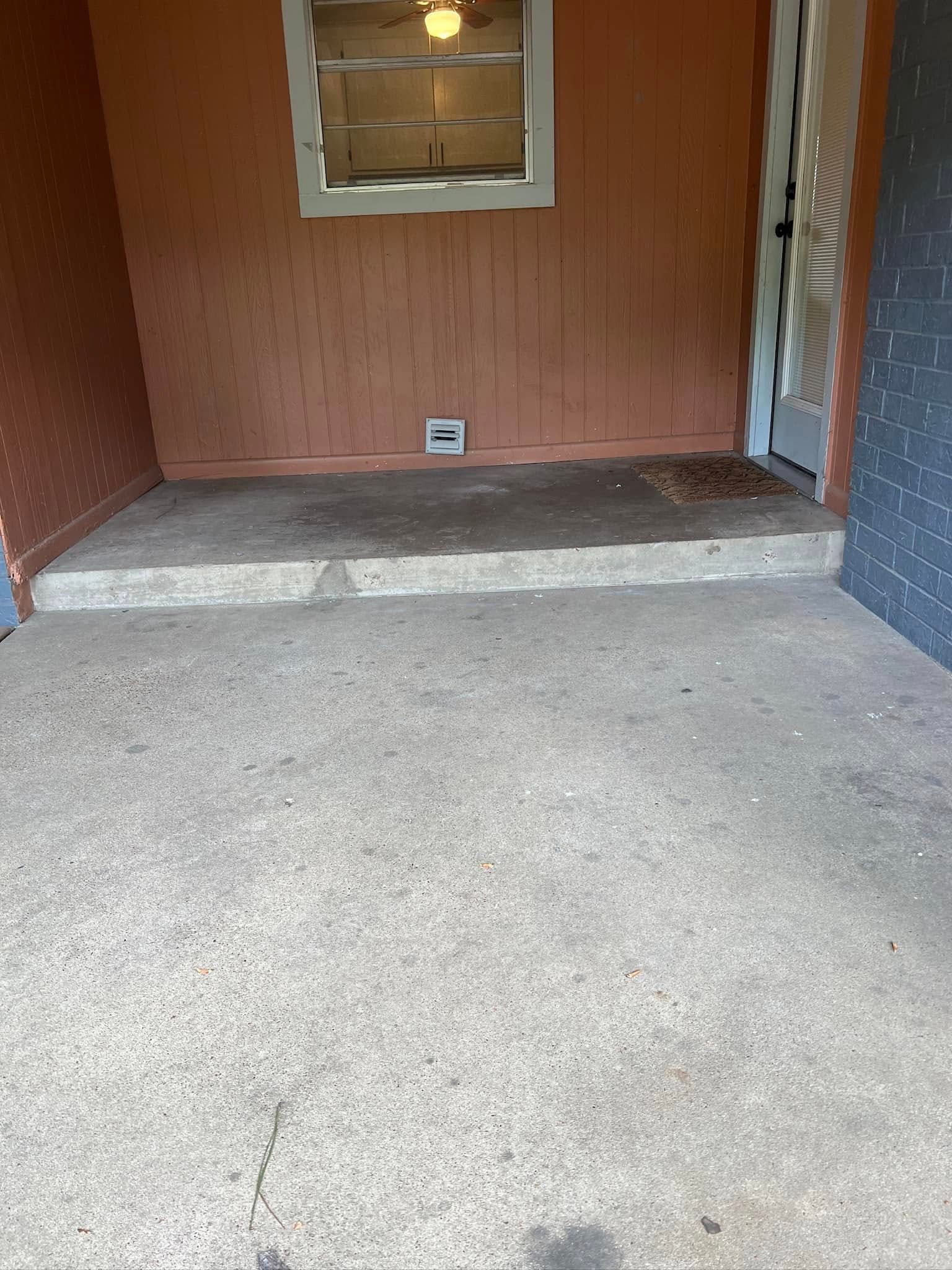 Concrete patio with a step leading to a doorway and a window. The wall is light orange.
