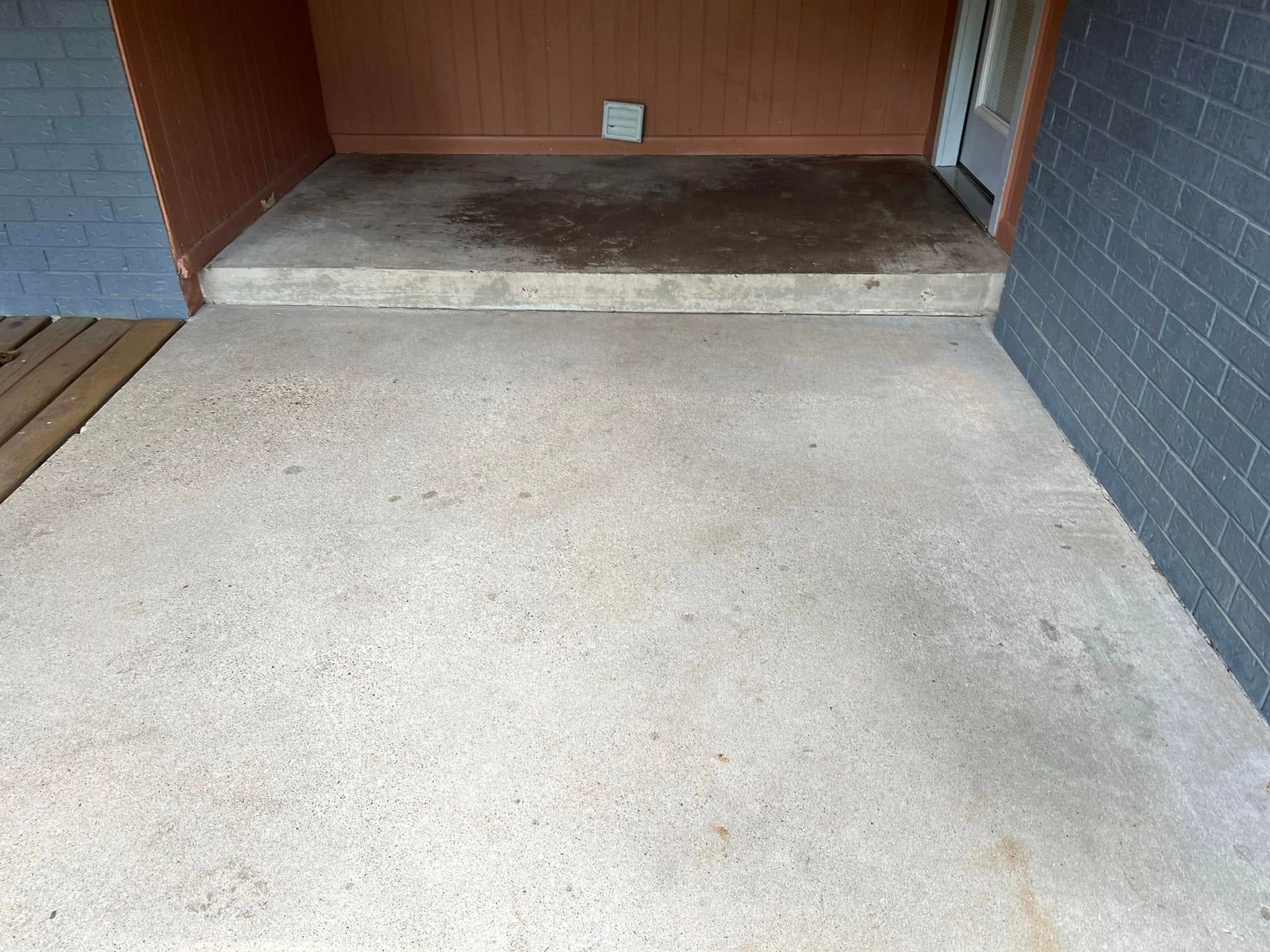 Concrete patio with a step leading to a raised area with a door and wooden paneling.