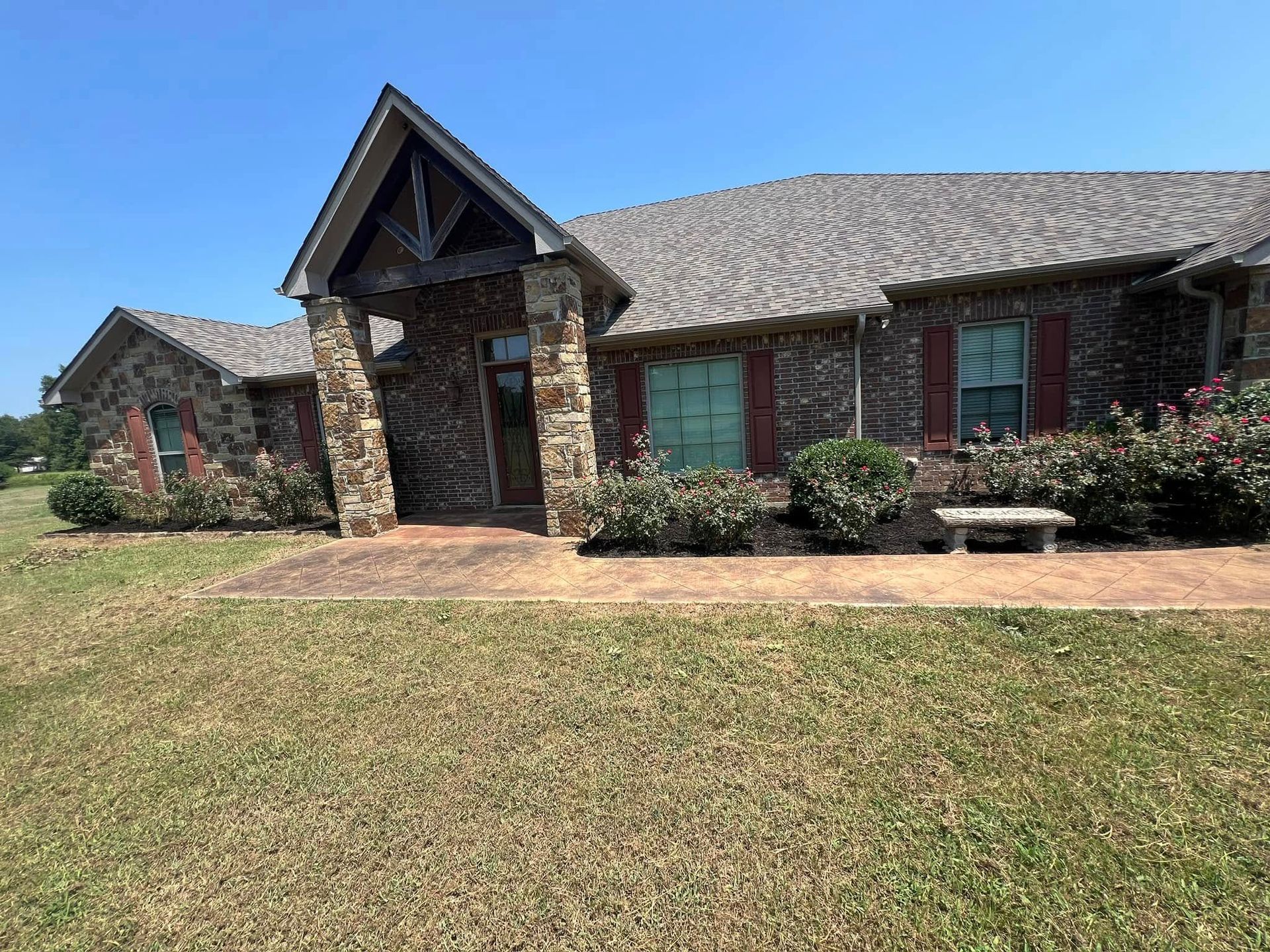 Brick house with brown roof, columns, and landscaping, on a sunny day.