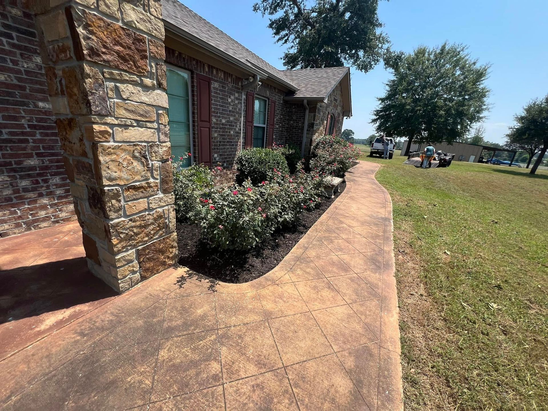 Brown stone house with a concrete walkway and flower beds.
