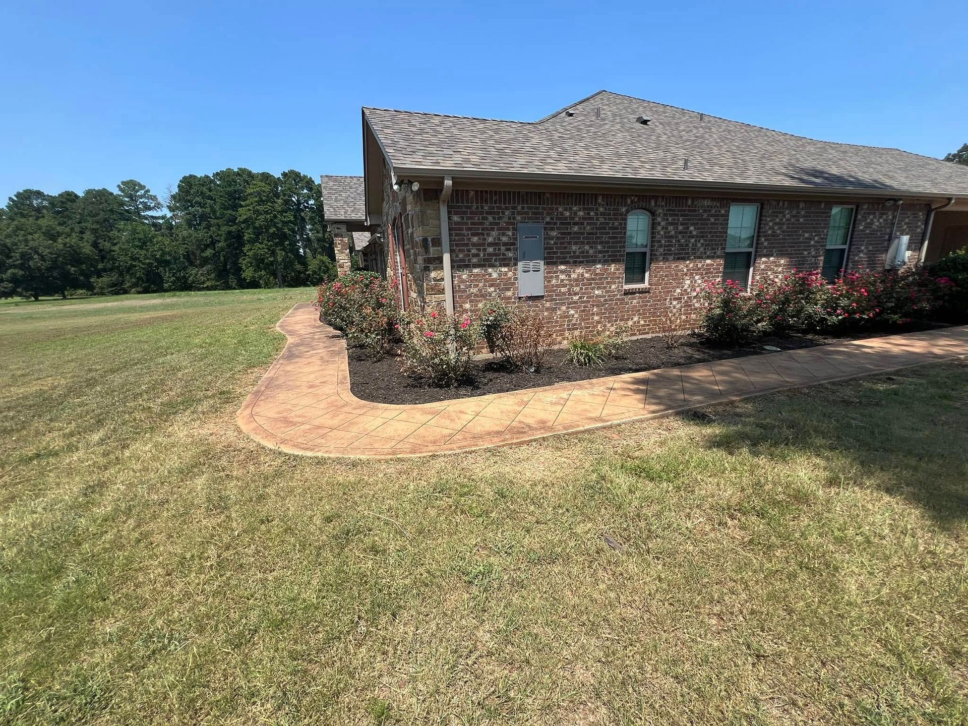 Brick house with a flower bed, brown roof, and green lawn.