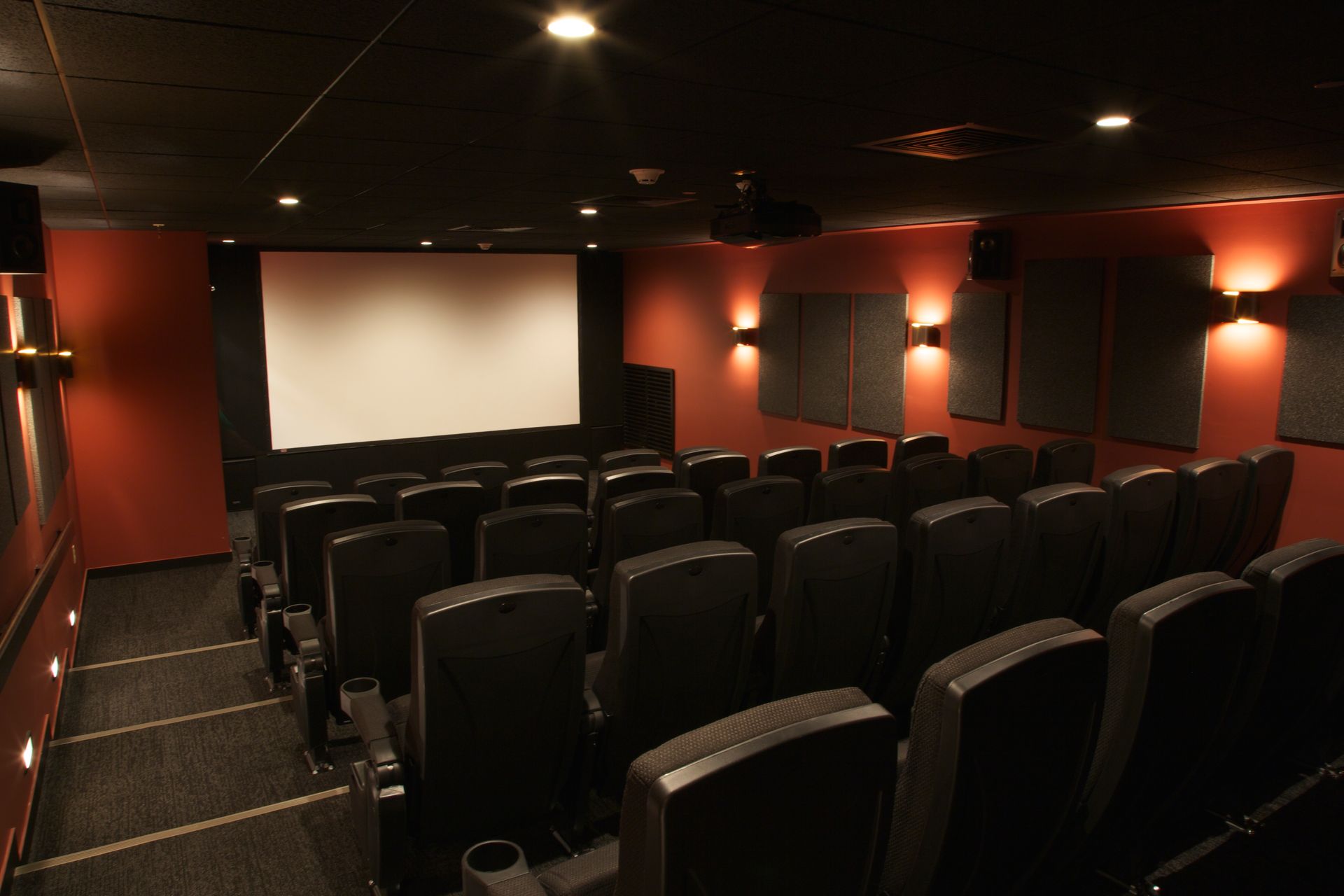 An empty movie theater with black seats and a large screen
