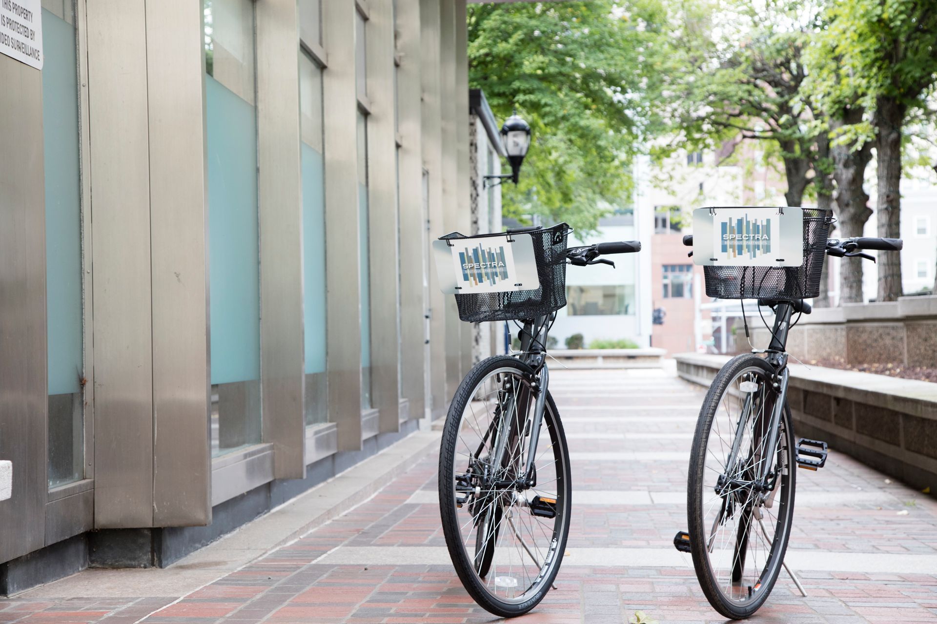 Two bicycles with baskets are parked on a sidewalk in front of a building.