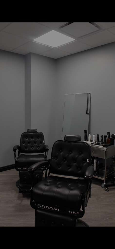 Two black barber chairs in a gray-walled salon with a mirror and a light fixture.