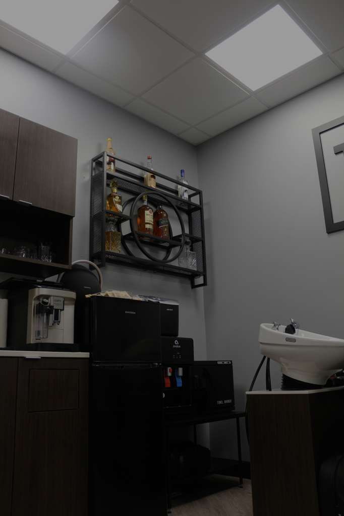 A gray-walled room with dark cabinets, a coffee machine, and a printer. A shelf holds bottles.