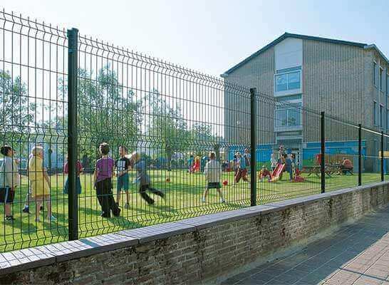 Un grupo de niños está jugando en un patio de recreo detrás de una valla.
