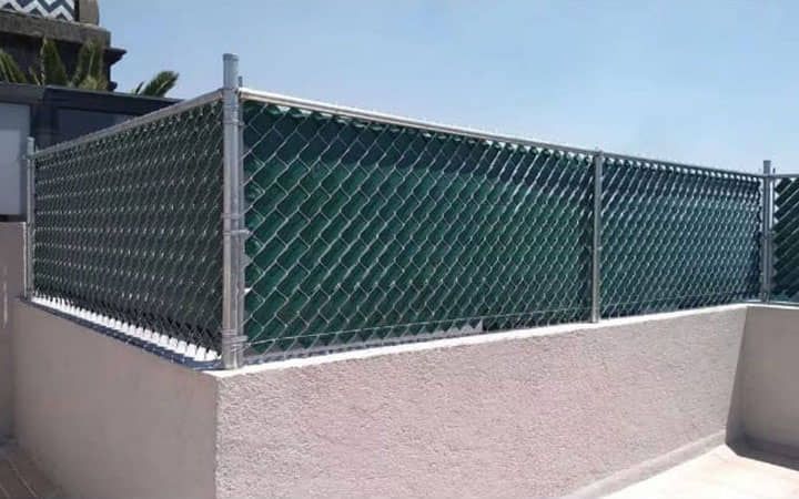 Una cerca de alambre de cadena con una tela de sombra verde adherida a ella.