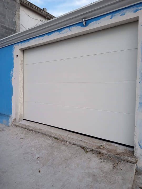 Una puerta de garaje blanca está delante de una pared azul.