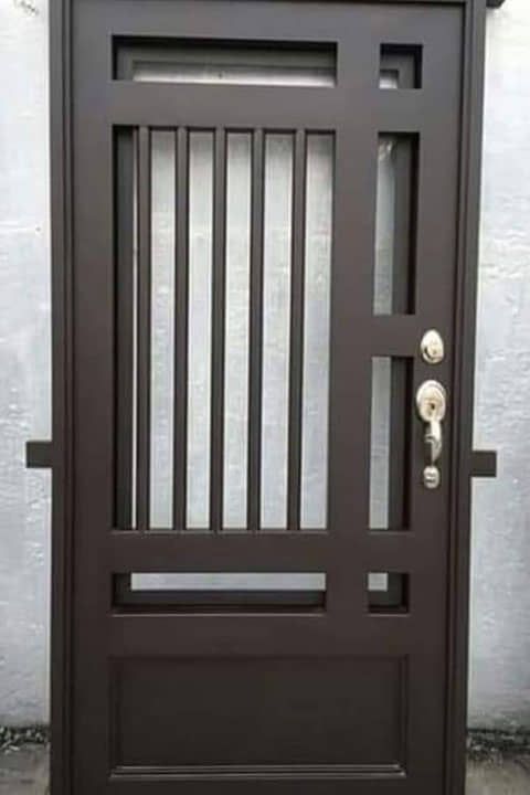 Una puerta de metal marrón con una ventana de vidrio se encuentra frente a una pared blanca.