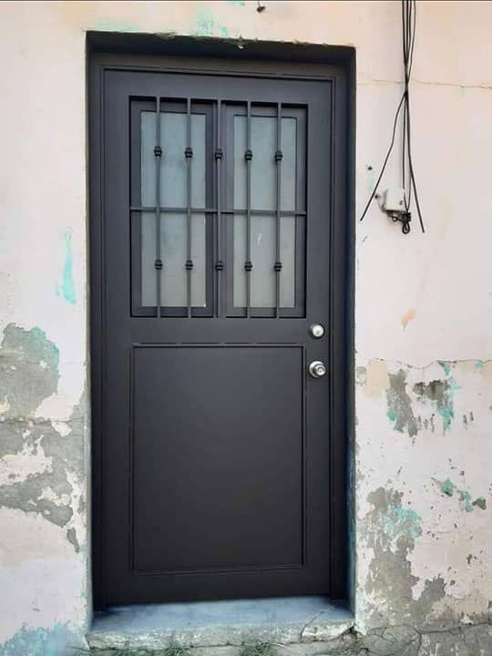 Una puerta negra está en una pared blanca con pintura descascarada.