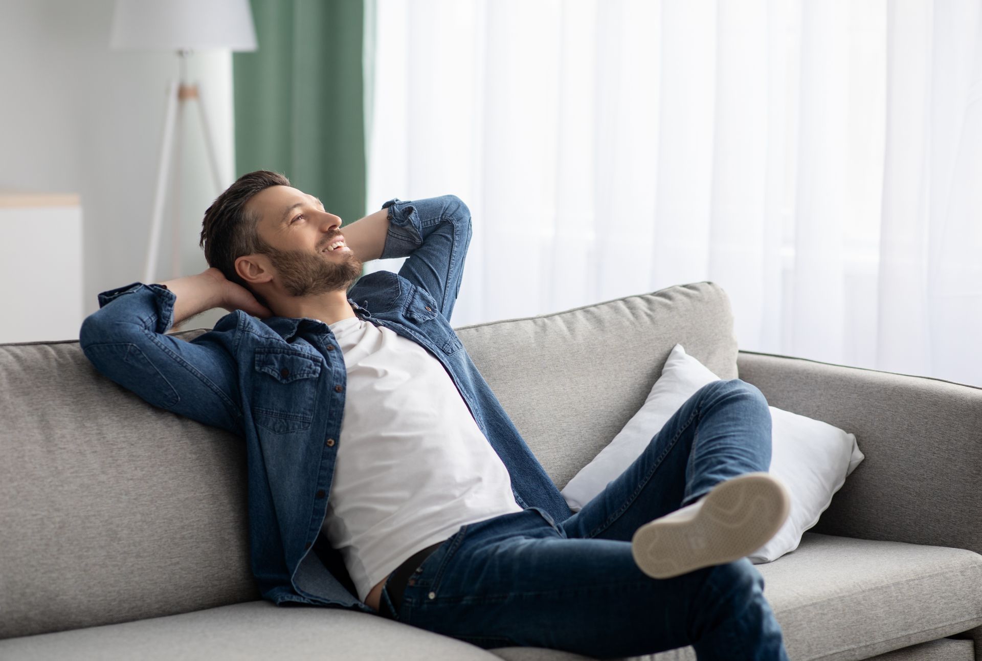Man relaxing on a couch, smiling with hands behind his head, looking up.