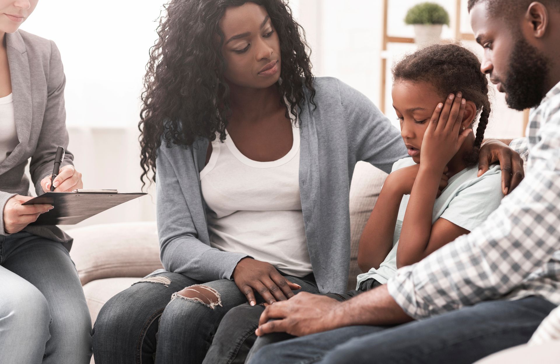 Family in therapy session; parents comfort a distressed child while a therapist takes notes.