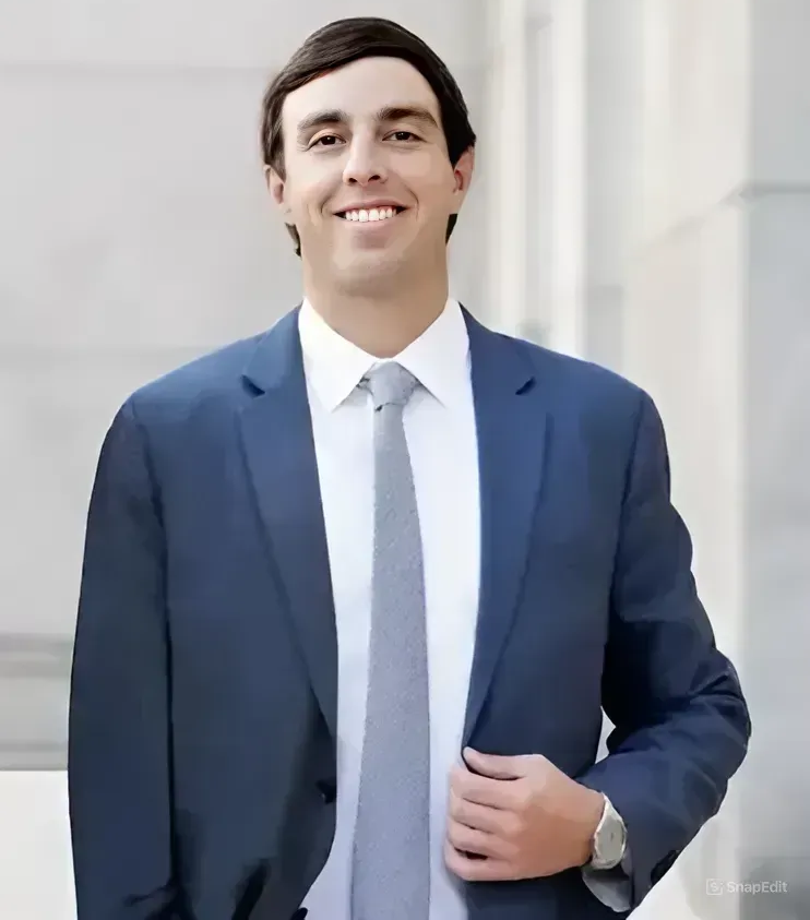 A person in a blue suit, white shirt, and grey tie smiling at the camera in an outdoor setting.