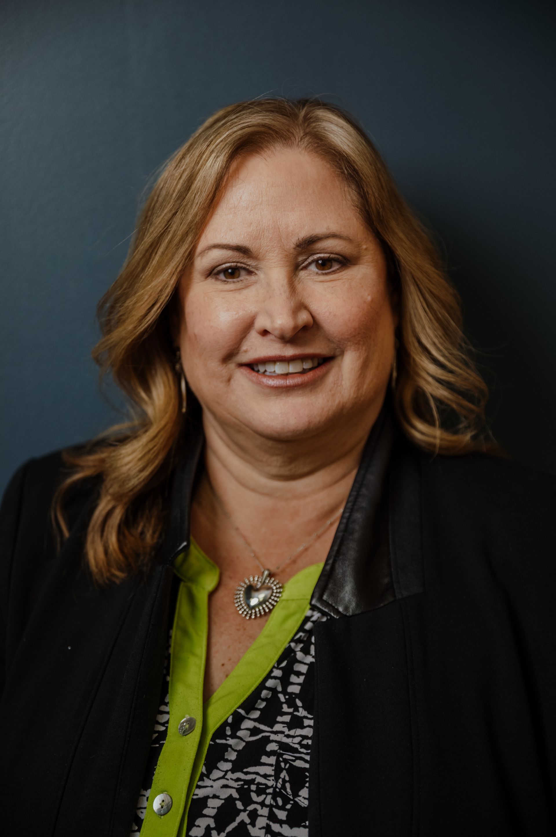 A woman wearing a black jacket and a green shirt is smiling for the camera.