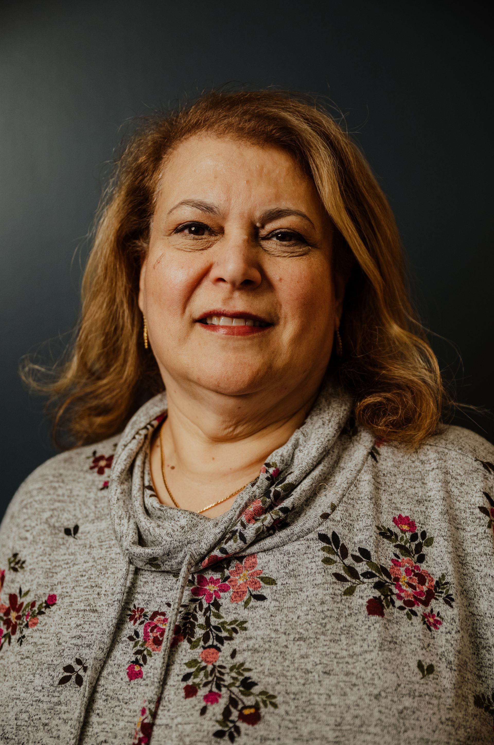 A woman is wearing a floral sweater and smiling for the camera.