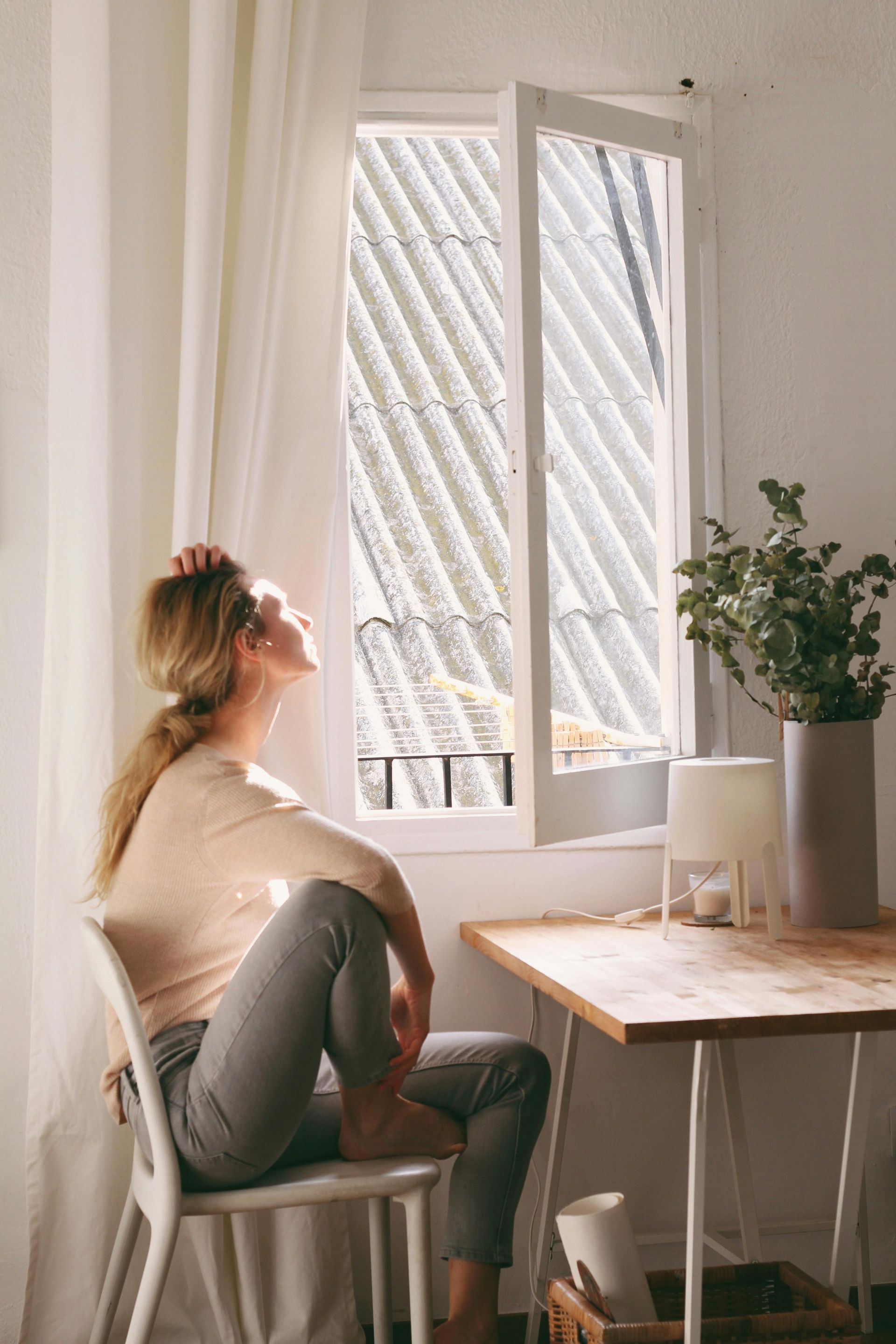 A woman is sitting in a chair looking out of a window.