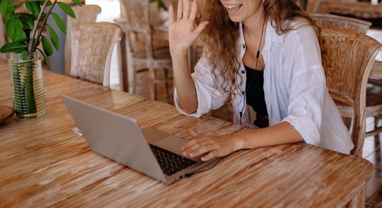 A woman is sitting at a wooden table using a laptop computer.