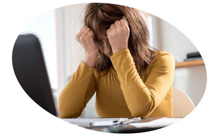 A woman is sitting at a desk with her head in her hands.