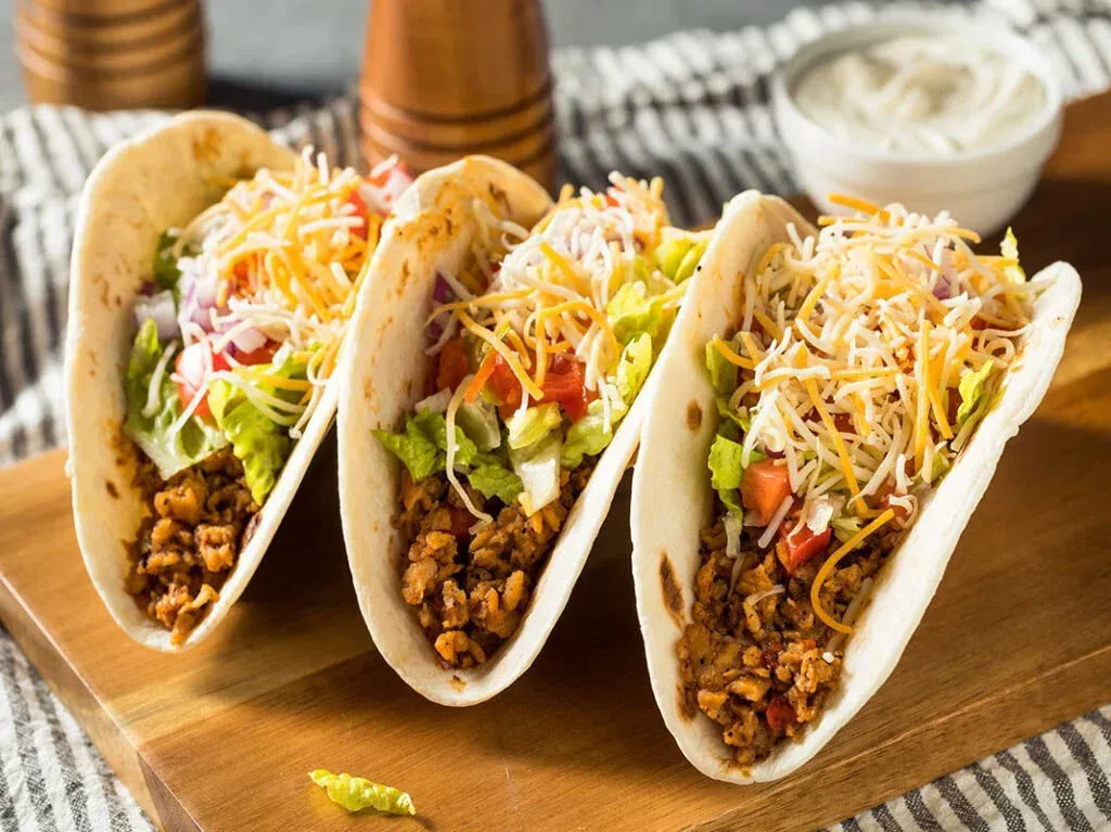 Three tacos are sitting on a wooden cutting board.
