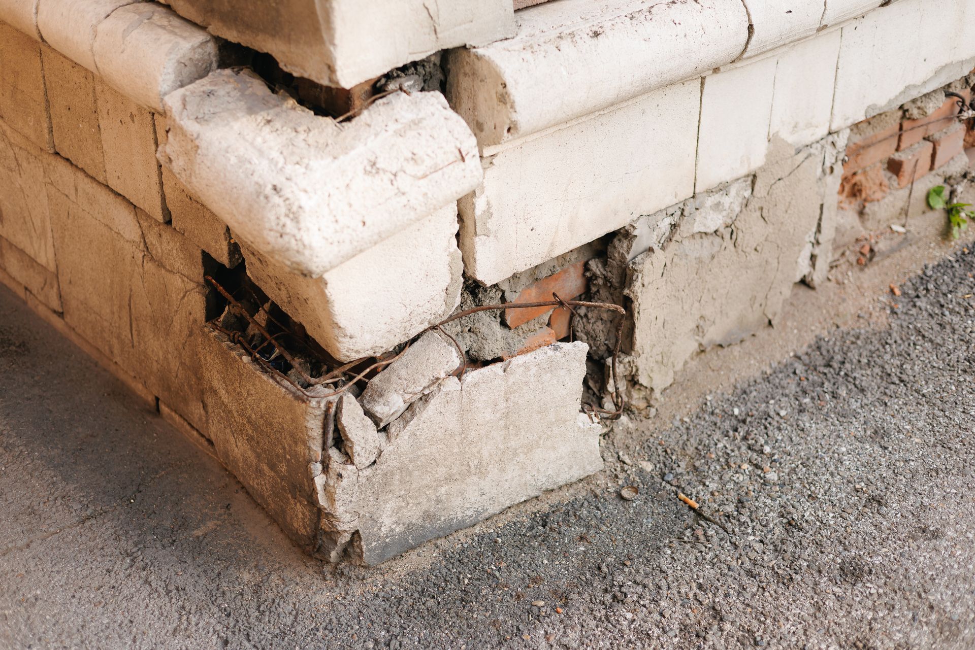 Cracked and crumbling concrete foundation corner showing exposed bricks and structural damage.