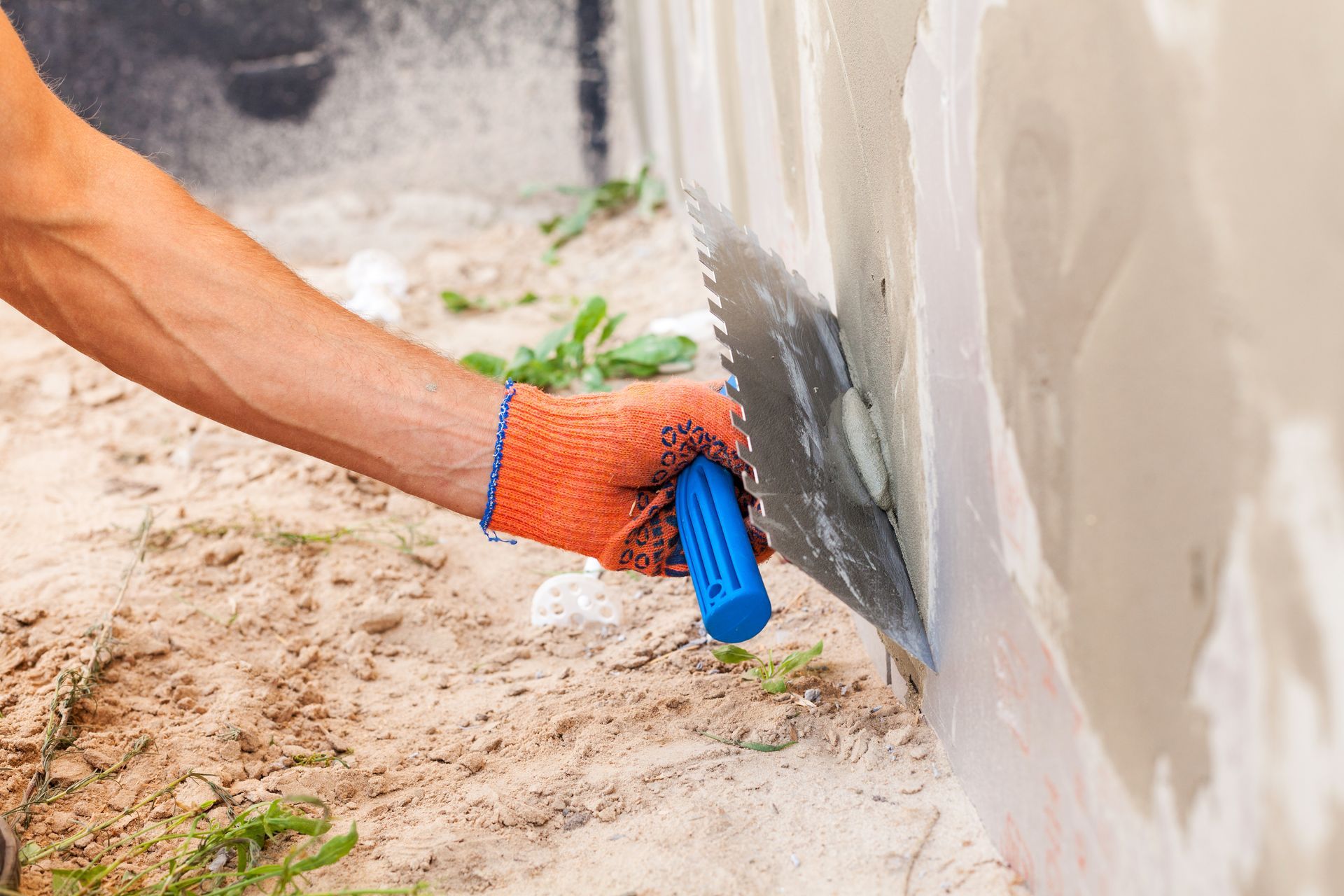 A foundation repair worker applying mortar to a cracked exterior wall.