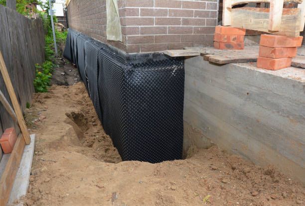 Black membrane applied to exposed foundation wall during basement waterproofing work.